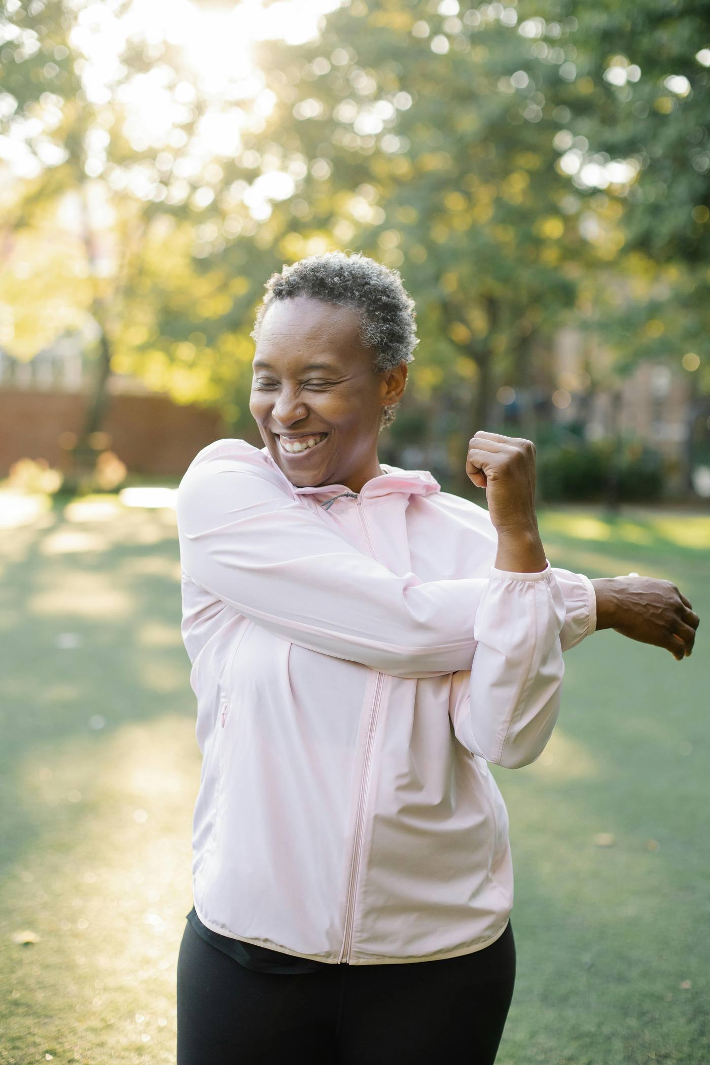 An older woman stretching outdoors, laughing in the sunlight